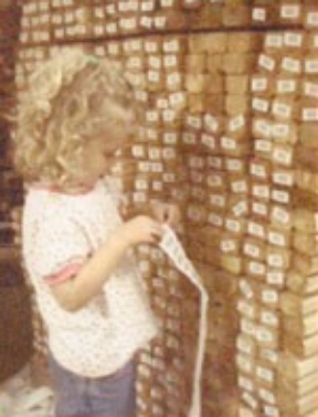 A young girl stands beside a stack of wooden blocks, showcasing her curiosity and potential for creativity.