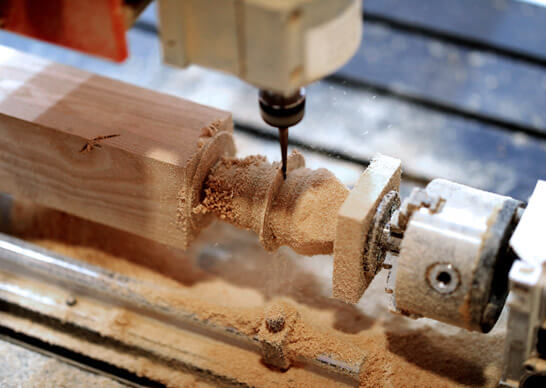 A drill being used on wood to carve a spindle.