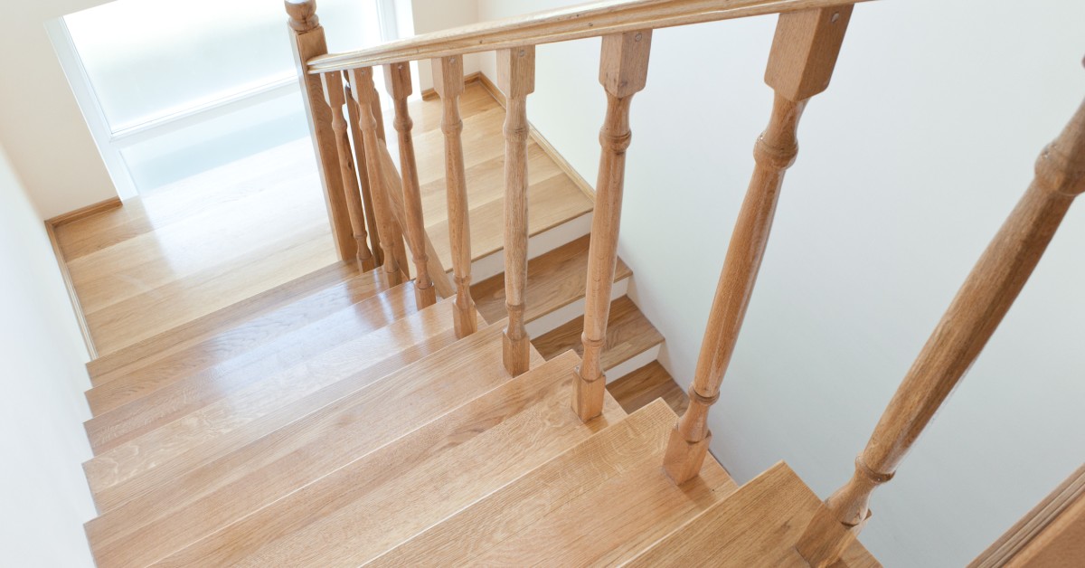 A two-story wooden staircase inside of a home. The spindles have decorative accents on the top and bottom.