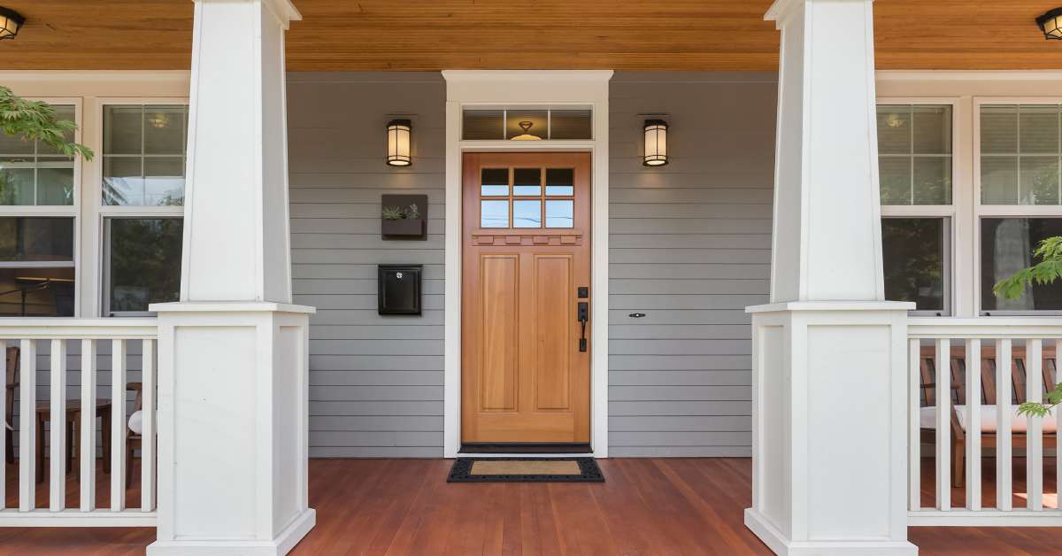 A gray home with a covered front porch and large columns flanking the front door. The porch is made from wood planks.