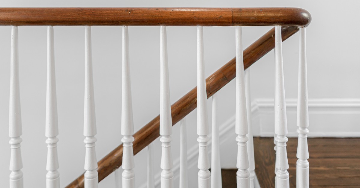 A close-up view of an interior staircase in a bright space. The railing is wooden and the detailed spindles are white.