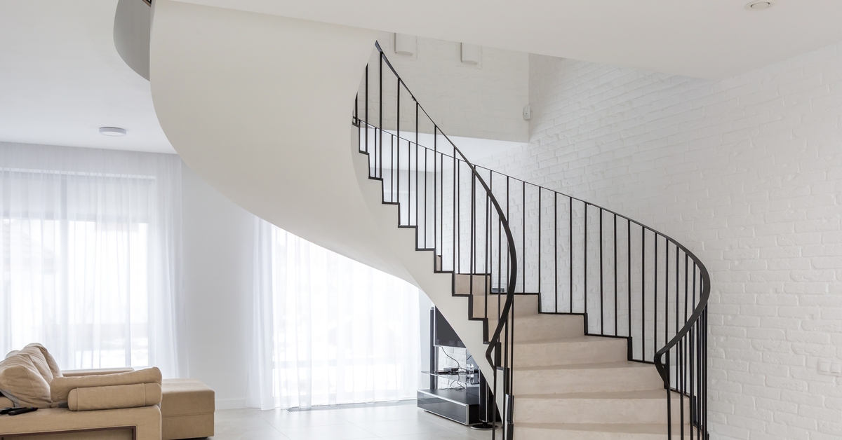 A spiral staircase in the middle of a modern room with white walls and a tile floor. The staircase has a black railing.