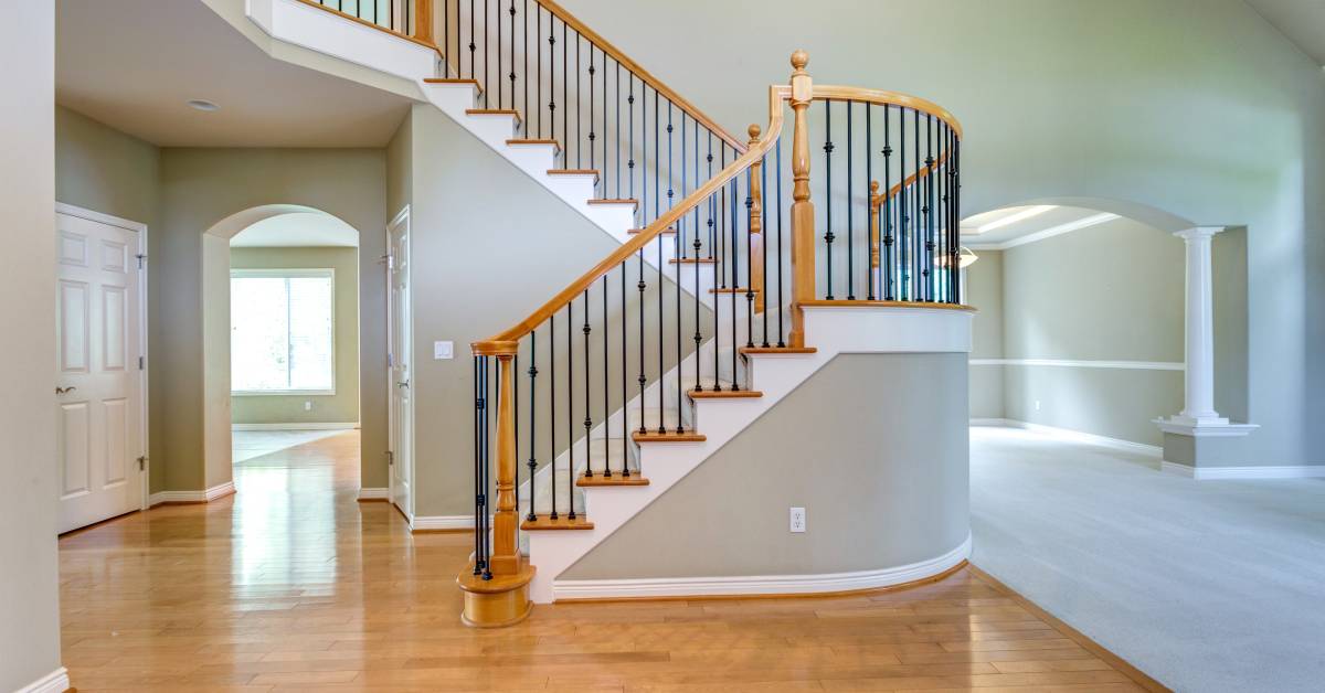 A large, empty traditional house with a staircase in the foreground leading to the second floor.