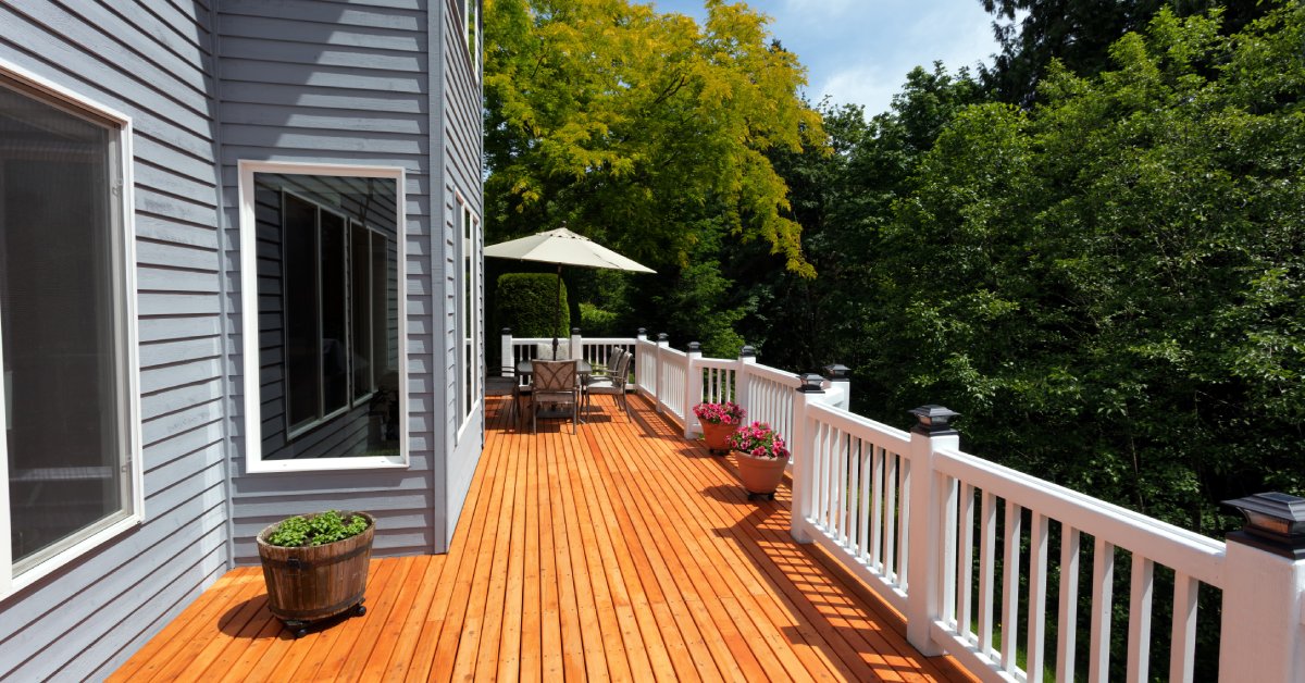 A back porch with a brand-new red cedar wood patio and white railings around the entire edge against a blue two-story home.