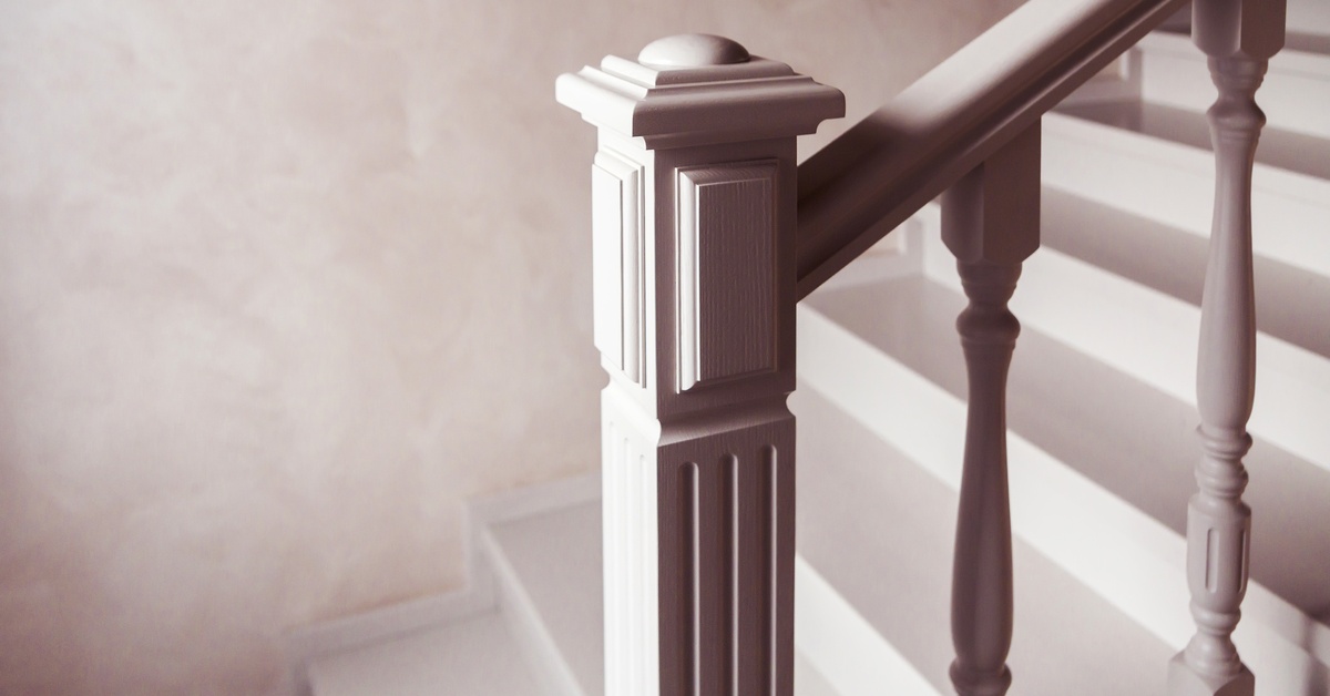 A white staircase features white steps, a boxed newel post, a railing, and spindles against a whitewashed wall.