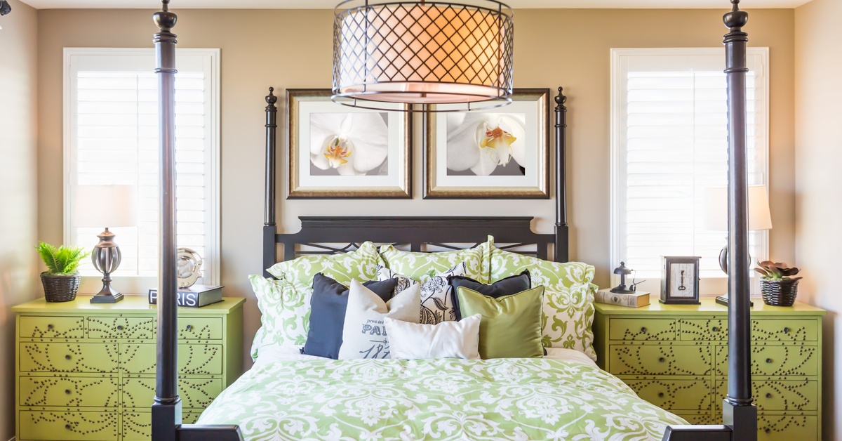 A traditional room features a dark wood four-poster bed with green bedding and matching green nightstands by the windows.