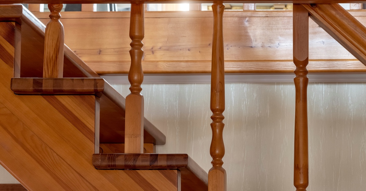 The side view of a tan, wooden staircase. It features decorative wooden spindles with carved grooves.