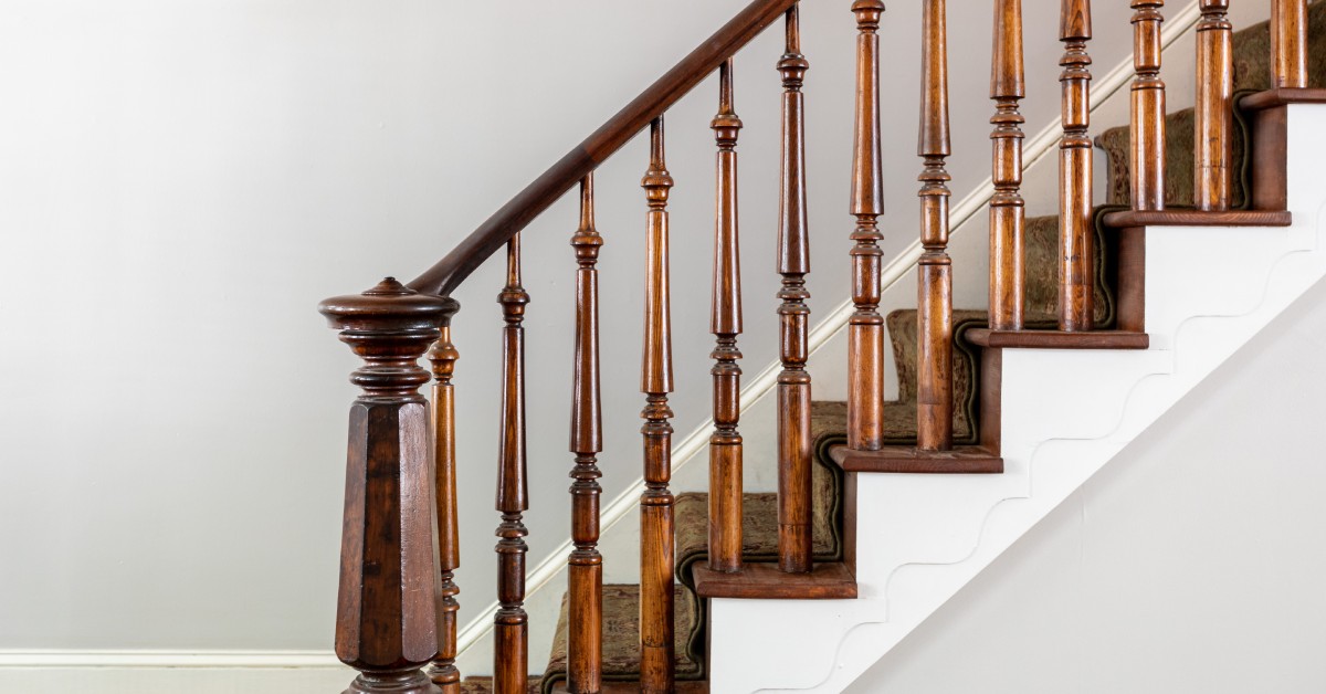 An Italianate-style staircase features dark carved wood balusters and railings against gray walls with white trim.
