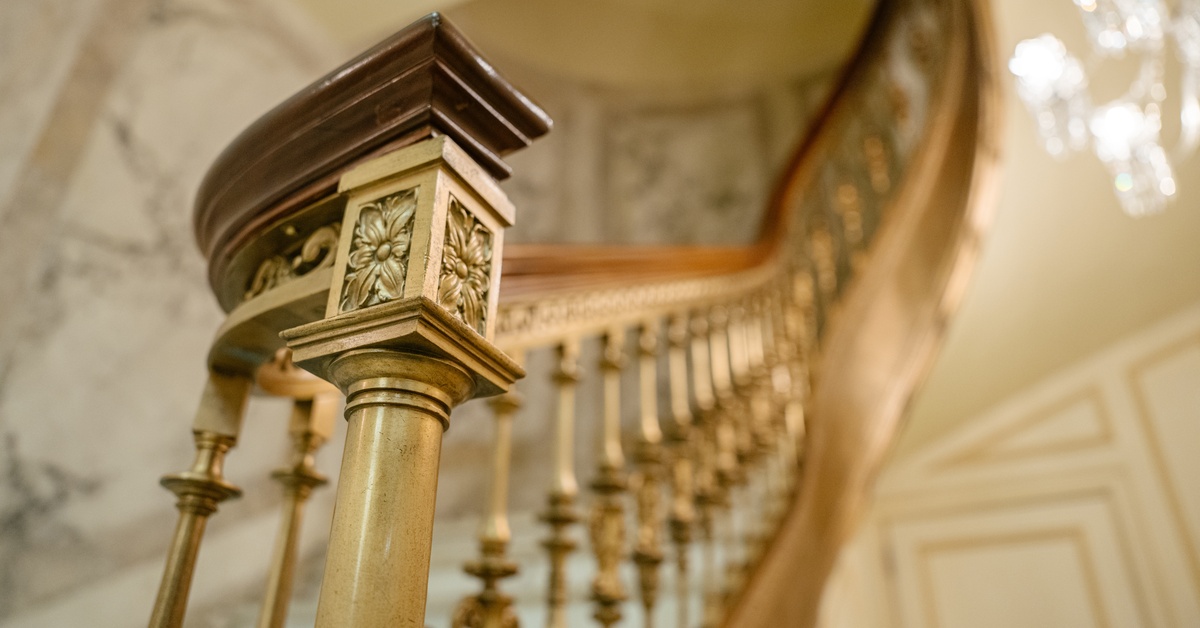 Ornate curved staircase with carved wooden handrail and decorative metal balusters in an elegant interior setting.