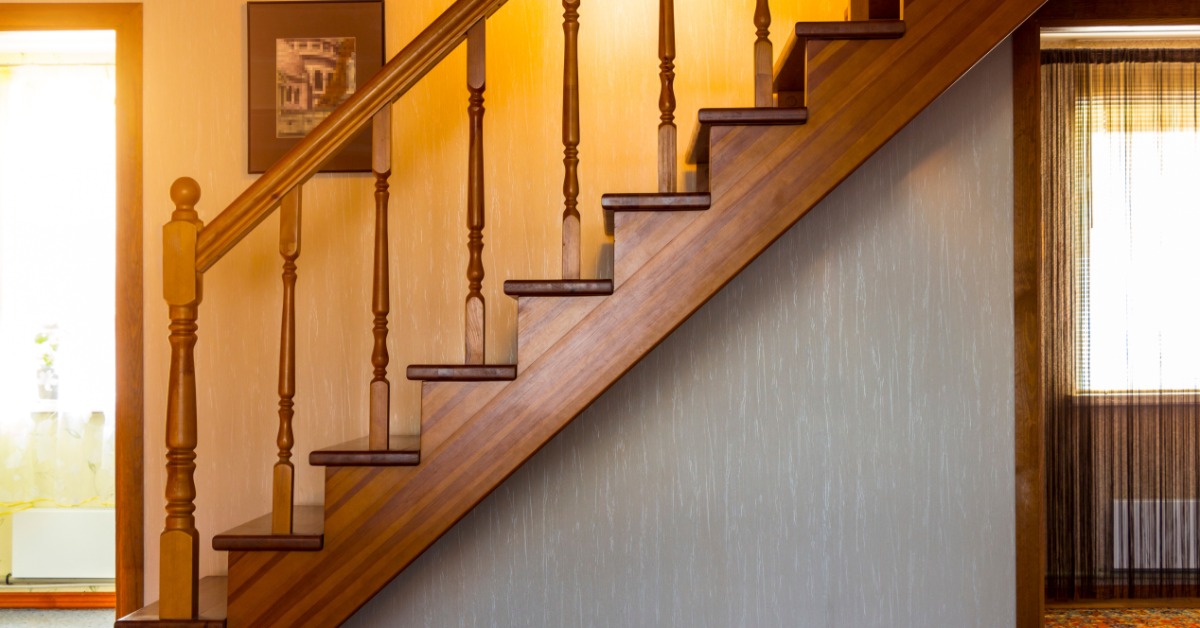 A wooden staircase with decorative railings runs along an interior wall inside a warmly lit home hallway.