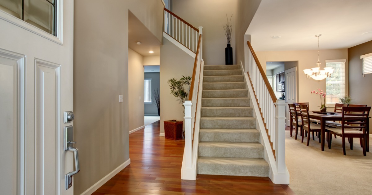 Bright home entryway with carpeted staircase, hardwood floors, and dining area in a modern two-story interior.