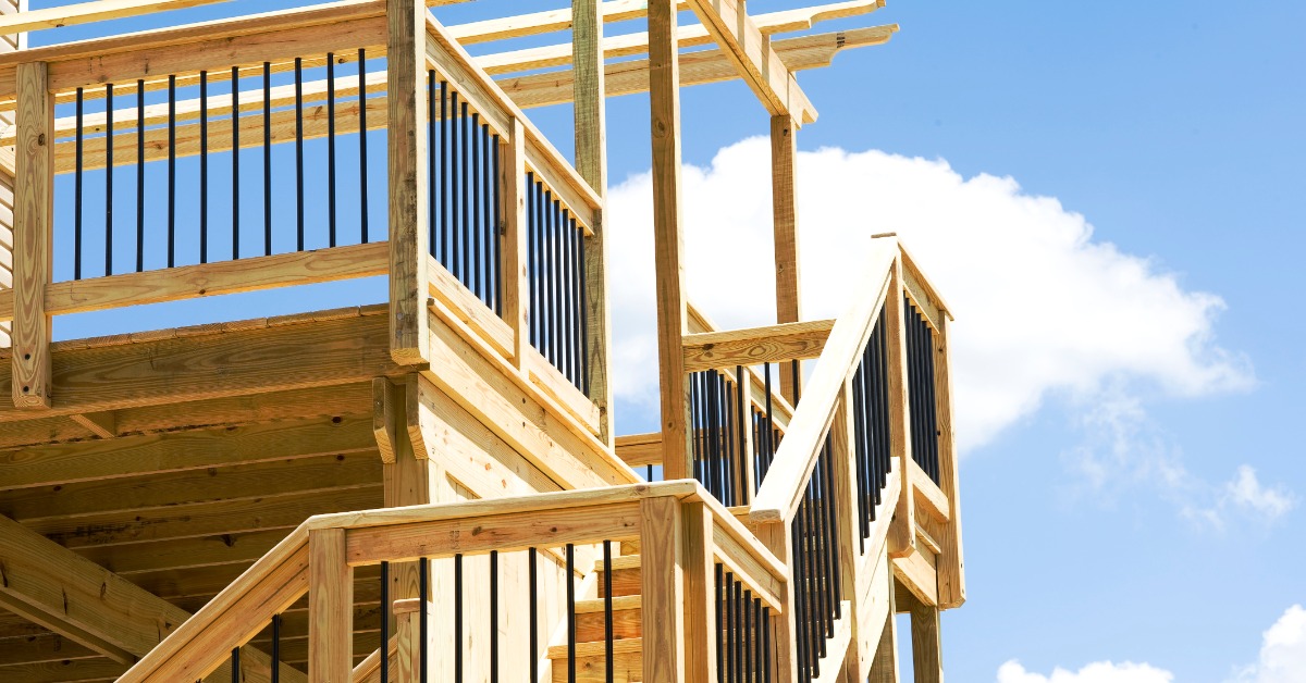 A wood deck under construction with exposed railing connections, stair rails, support posts, and black metal balusters.