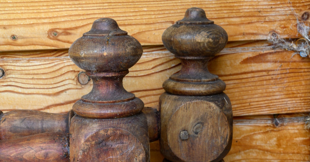 Two weathered wooden finials with turned details stand against a wood wall, showing visible signs of age and wear.